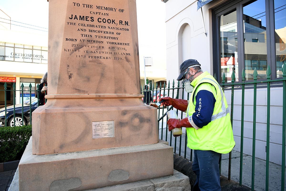  A worker paints over graffiti on a Captain Cook statue