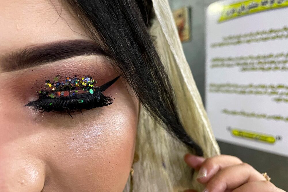 Gender apartheid in Afghanistan - Photo: an Afghan woman shows off her party make-up (sequins) in close-up, after lifting her veil.