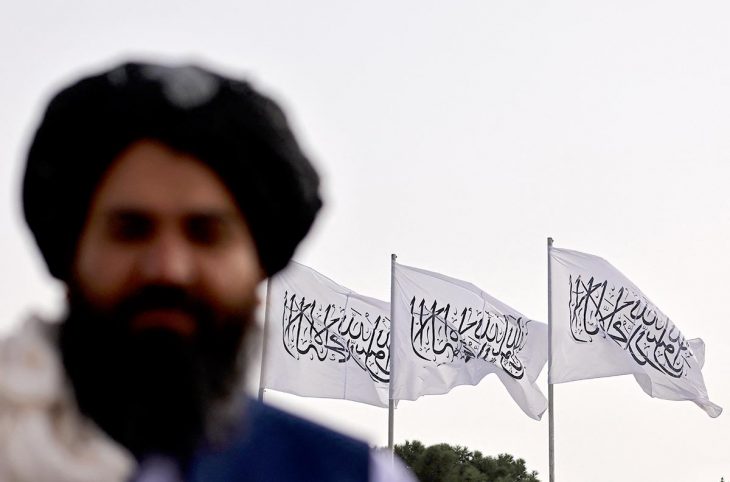 Taliban fighter posing in front of Taliban flags