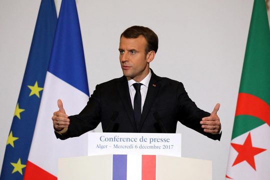 Emmanuel Macron prononce un discours à Alger entouré des drapeaux français et algérien.