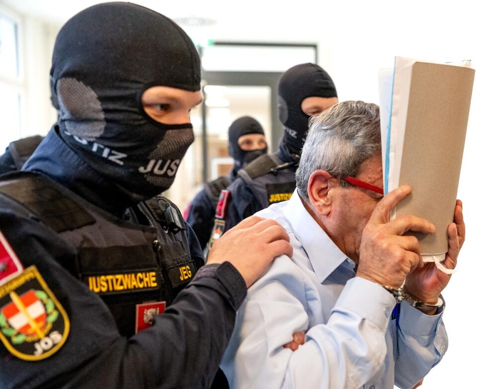 L’ex-général syrien Khaled al-Halabi se couvre le visage au début de son procès à Vienne, en Autriche. Lundi 6 juillet, al-Halabi a été condamné, aux côtés d’un ancien officier de police syrien, pour avoir torturé des opposants au dirigeant déchu Bachar al-Assad. Photo : © Joe Klamar / AFP Syrie : l'ancien général syrien Khaled al-Halabi a été condamné en Autriche pour des allégations de torture, en vertu de la compétence universelle. Photo : Halabi est escorté par des policiers autrichiens et se cache le visage.