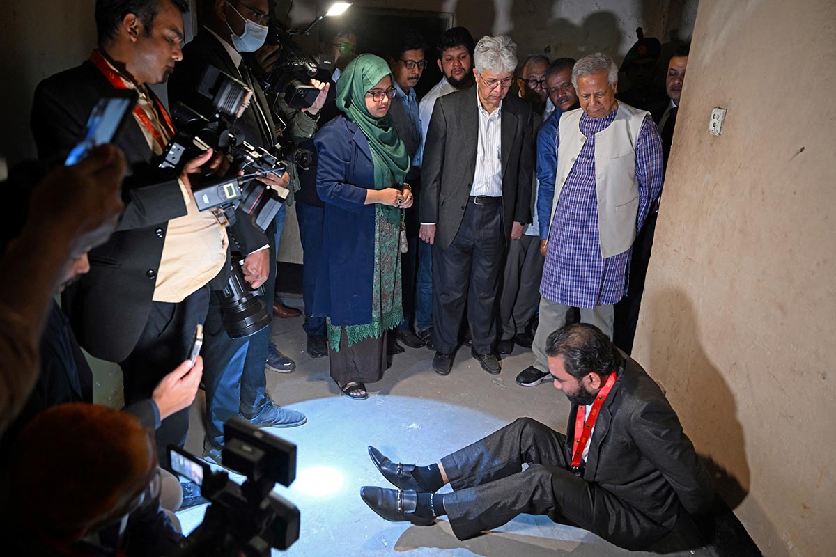 Un ancien détenu et victime est assis par terre contre un mur, mimant et racontant son calvaire au conseiller principal du gouvernement provisoire, Muhammad Yunus, lors de la visite de ce dernier à la « Maison des miroirs » (Aynaghar) au Bangladesh.