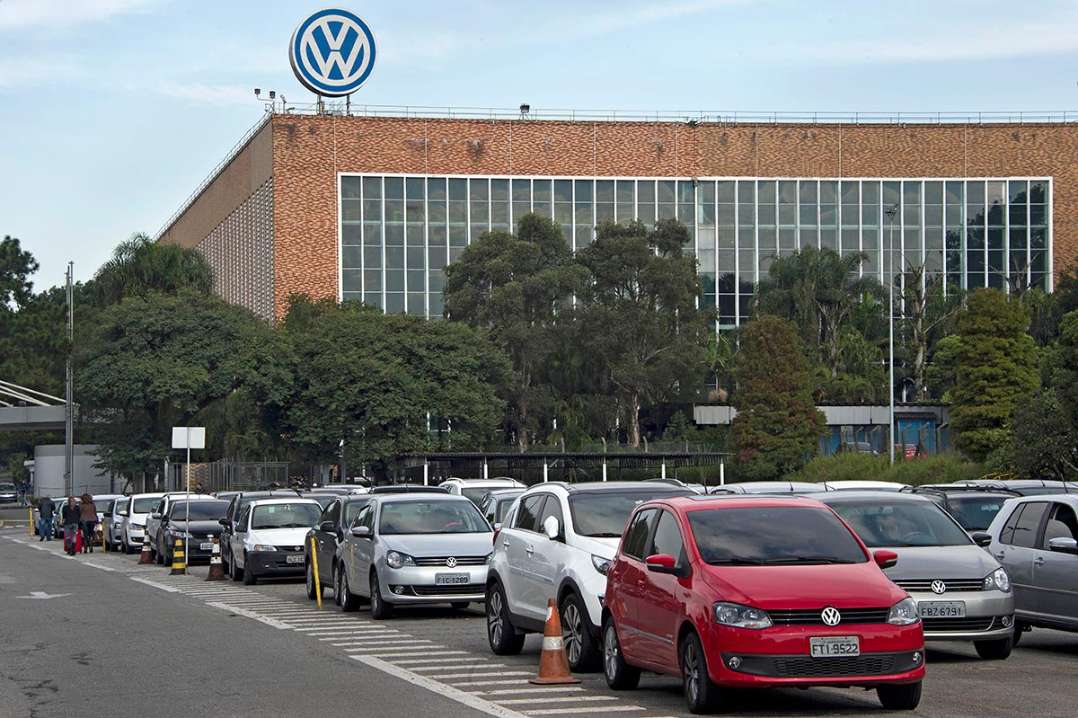 De nombreuses voitures de la marque Volkswagen sont alignées devant une usine, située au Brésil, affichant le logo de la compagnie allemande.