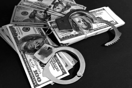 Business and international crimes. Could the Lafarge case (this cement company is on trial in France for crimes committed in Syria) cause lasting concern for other multinationals suspected of being involved in war crimes or crimes against humanity? Photo: a pair of handcuffs is placed on bundles of banknotes (US dollars).