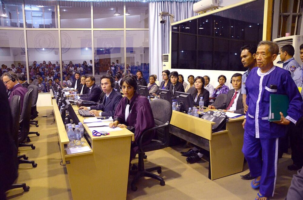 L’accusé Kaing Guek Eav, alias Douch (debout à droite), ancien tortionnaire sous Pol Pot, entre dans le tribunal pour les Khmers rouges, à Phnom Penh, et passe devant de jeunes juristes, la plupart cambodgiens, travaillant au bureau du procureur. Photo : © Susan Banks Bien être du personnel dans les Tribunaux internationaux. Photo : audience en présence de l'accusé 'Douch' au Tribunal pour les Khmers rouges (Cambodge).