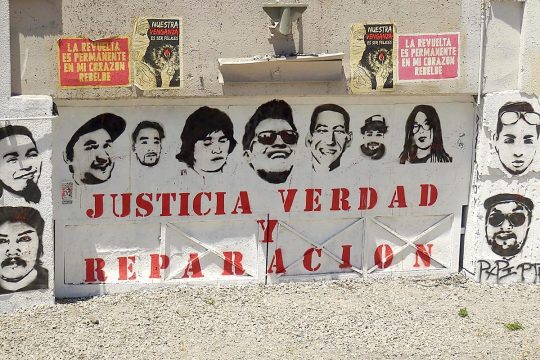 Dans une rue au Chili, une affiche collée sur un mur forme cette phrase : "Justicia, verdad y reparacion". Des portraits sont disposés au-dessus.