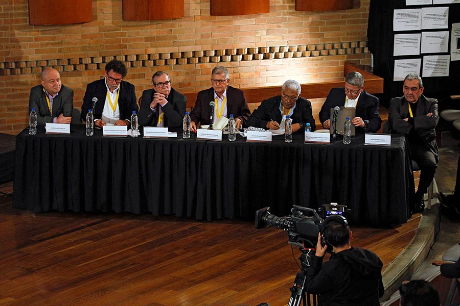 7 ex-FARC lors d’une audience de la JEP en Colombie En Colombie, 7 ex-membres des FARC ont été condamnés en 2025 pour crimes de guerre et crimes contre l'humanité. Photo : 7 personnes (dont une personne qui ne fait pas partie des 7 condamnés) sont assises devant une longue table, avec leurs noms inscrits devant eux.
