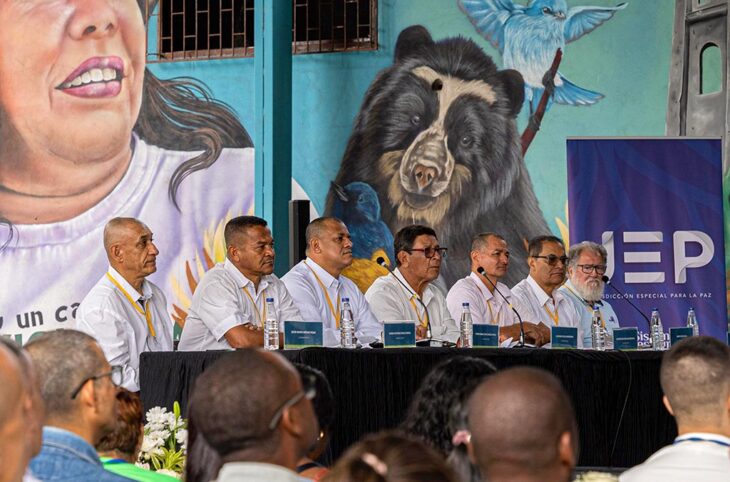 En Colombie, des victimes d'enlèvements se retrouvent face aux commandants FARC responsables de ces crimes. Photo : 7 anciens commandants de la guérilla sont assis, alignés devant un bureau et des micros, en chemises blanches et regardent devant eux. Derrière eux, une fresque murale représentant des hommes et des animaux.