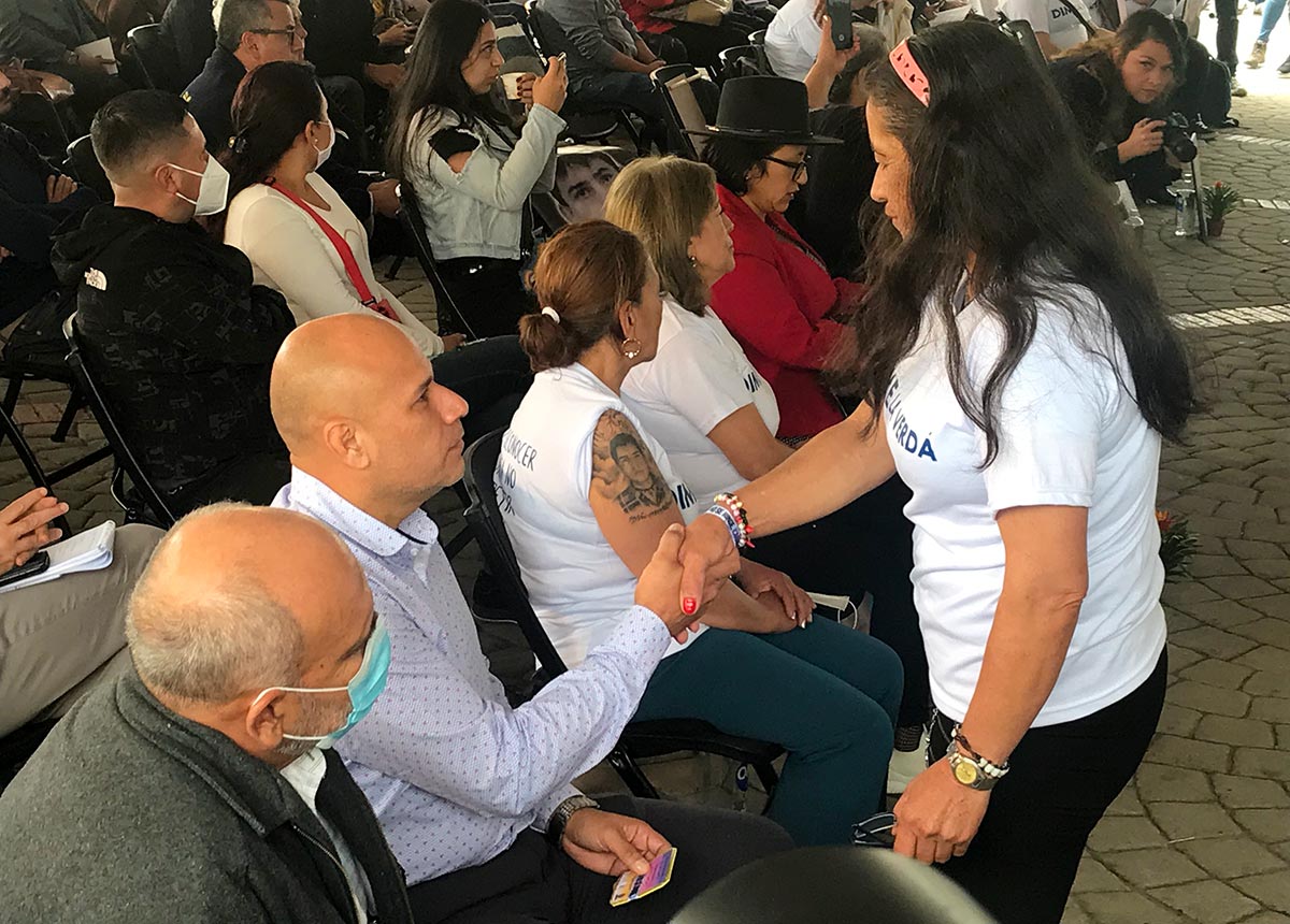 Una mujer (de pie) estrecha la mano de un hombre (sentado) durante una reunión, organizada por la Comisión de la Verdad de Colombia, entre madres y hermanas de víctimas del ejército colombiano y oficiales implicados en estos crímenes.