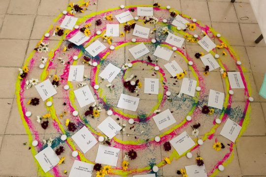 An installation in memory of the victims of the La Gabarra massacre in Colombia: a colorful spiral made of candles, flowers and sheets of paper on which the names of the victims have been written.