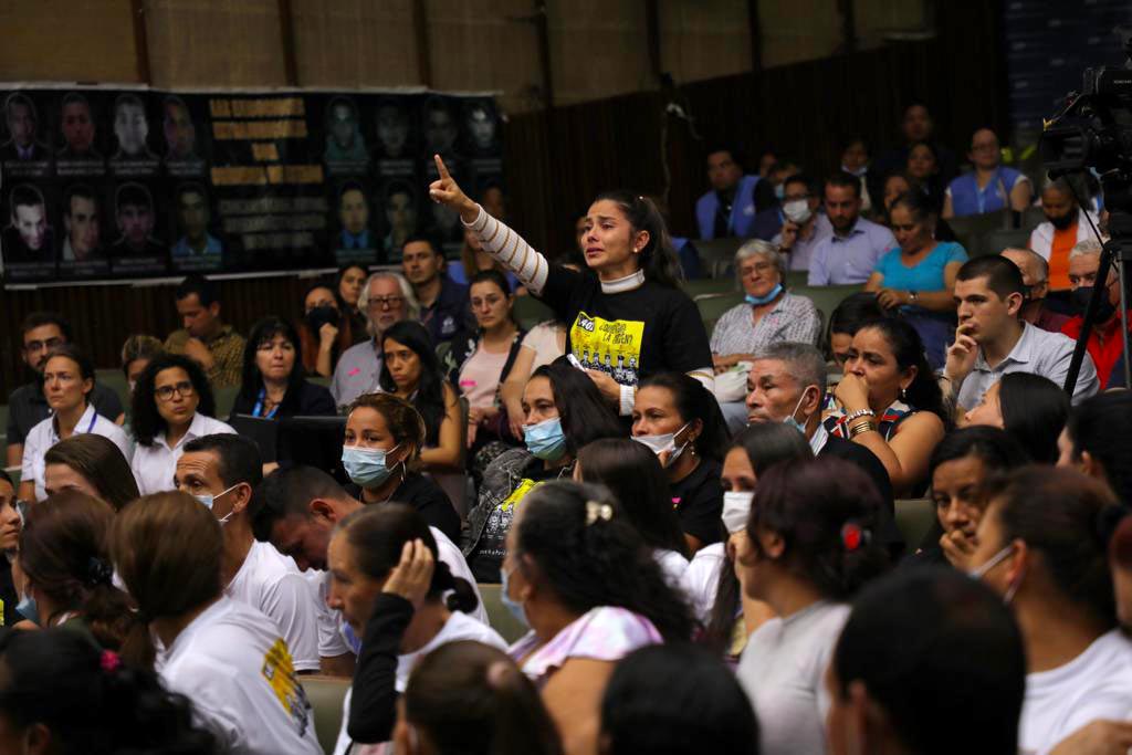 Soraida Navarro, de pie entre el público, levanta el dedo para hablar. Lleva una camiseta negra con un visual amarillo.