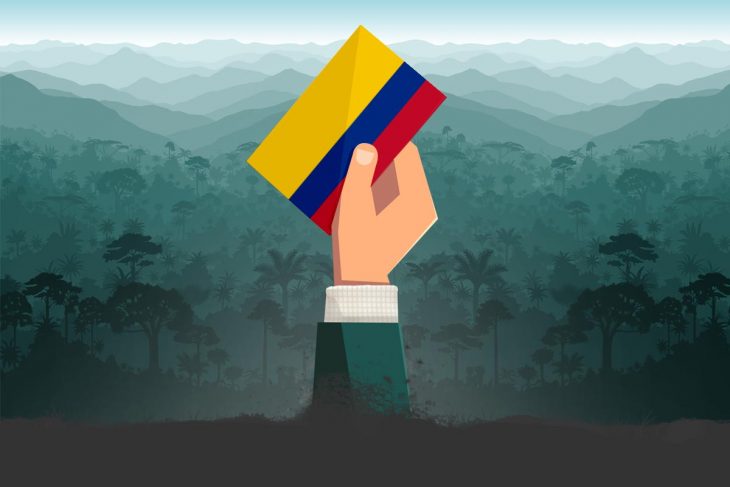 A hand emerging from the ground holds a ballot in the colors of the flag of Colombia
