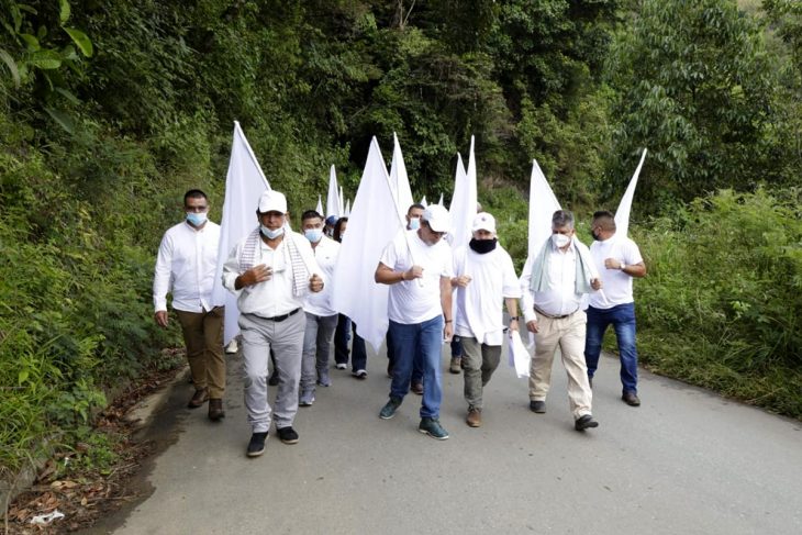 Former FARC members walk down a road dressed in white and carrying white flags.