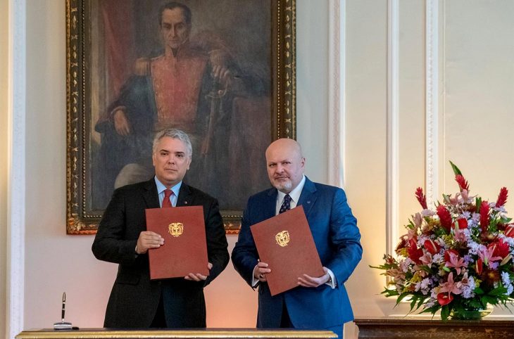 Iván Duque y Karim Khan posan con un documento en la mano. Detrás de ellos se exhibe un cuadro de Simón Bolívar.