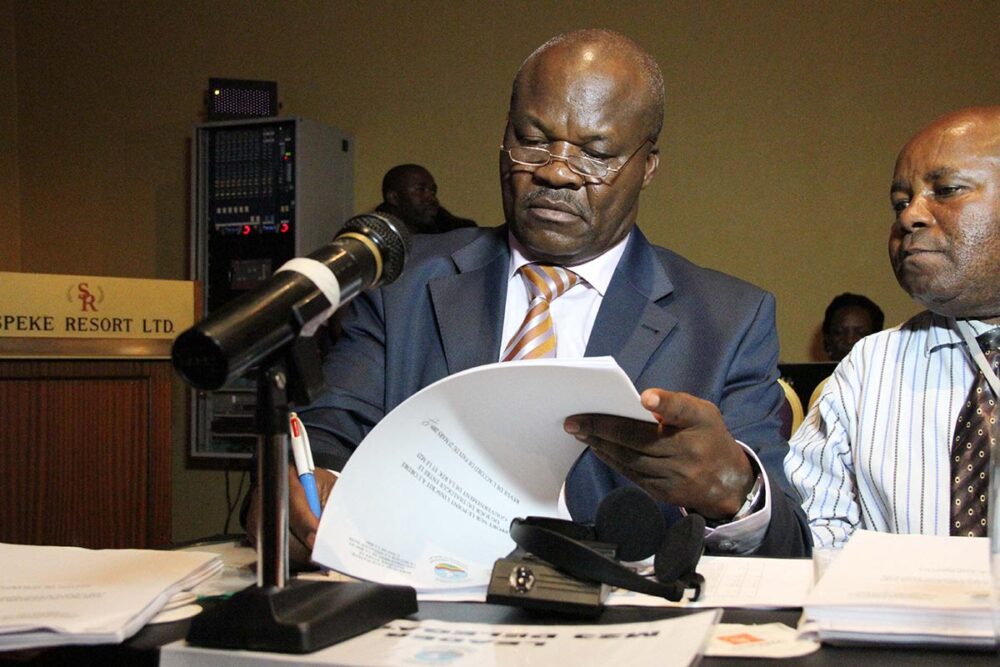 Procès de Roger Lumbala à Paris (France) pour des crimes commis en République démocratique du Congo (RDC). Photo : Lumbala est assis à un bureau en 2013, à côté d'un second personnage. Il signe un document.