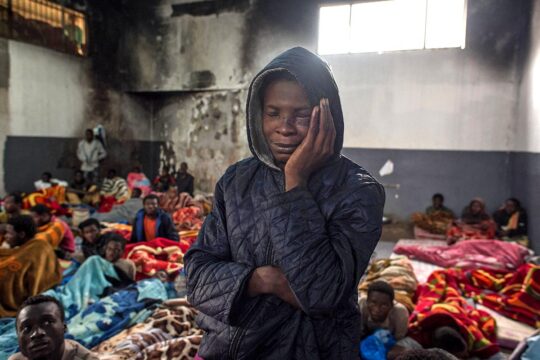 Entre l’Érythrée et les Pays-Bas, le calvaire des migrants victimes de trafic d'êtres humains. Photo : un migrant dans un centre de détention à Tripoli, en Libye, se tient debout avec une main sur la joue, semblant presque dormir.