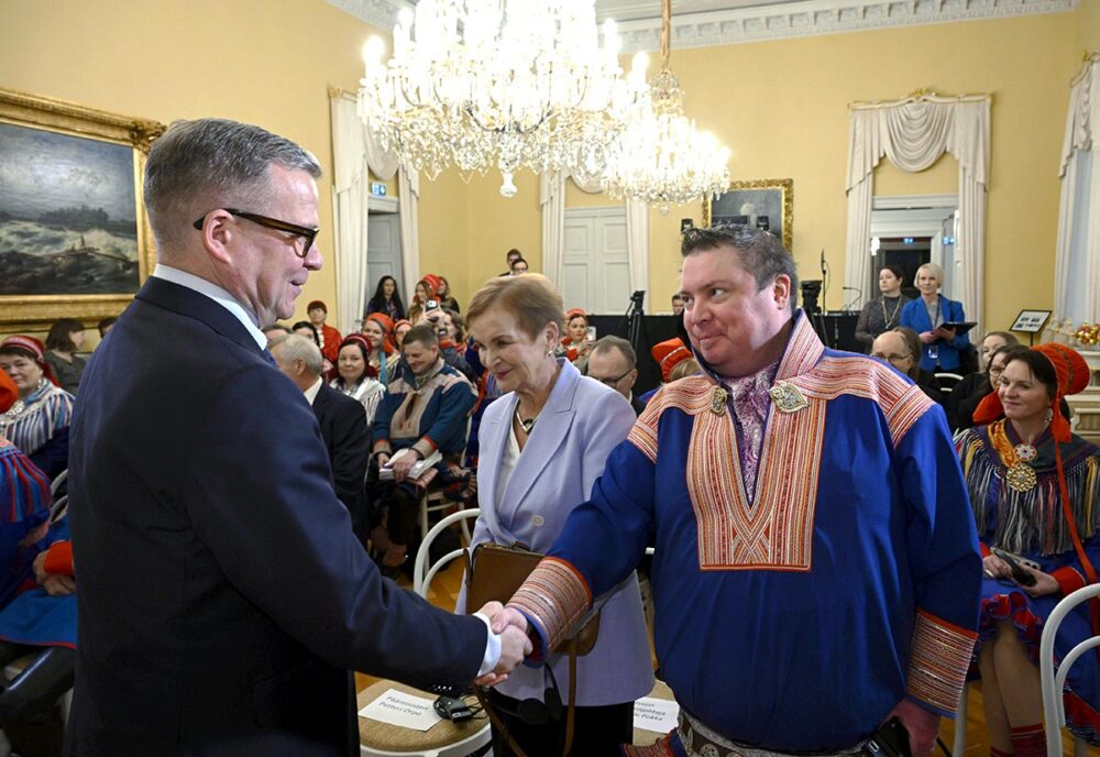 En Finlande, le premier ministre Petteri Orpo et Tuomas Aslak Juuso (du parlement Sami) se sont rencontrés pour la remise du rapport de la Commission vérité et réconciliation. Photo : Orpo et Juuso se serrent la main dans une salle de réception comble. Juuso porte les vêtements traditionnels samis.