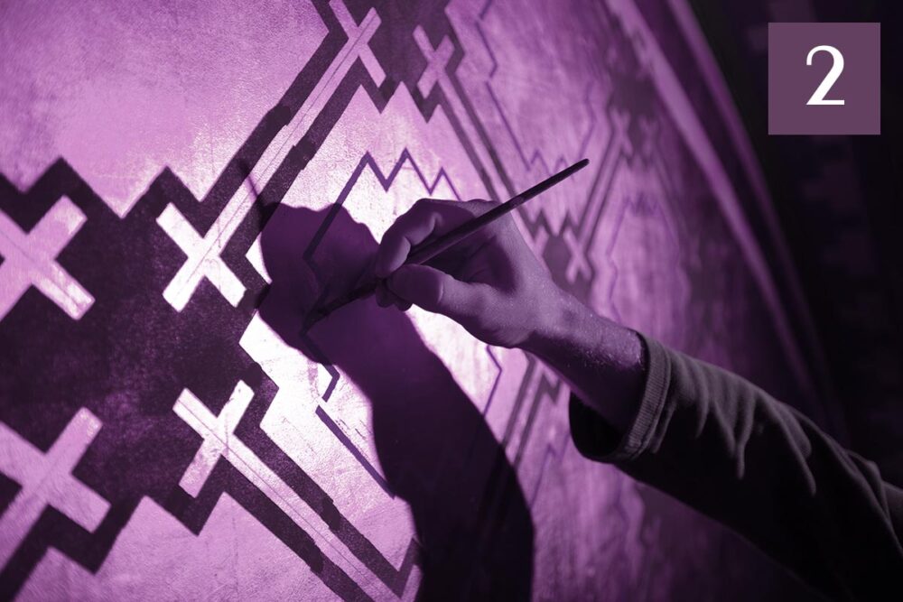 Réparations pour les victimes de l'Église de France. Photo : un peintre utilise un outil pour rénover une peinture murale où plusieurs croix catholiques sont représentées.