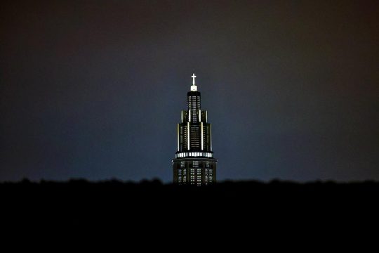 A church seen at night in France with some ornaments (a cross at the top) illuminated.