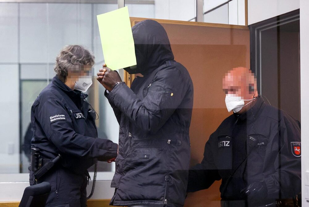 Bai Lowe is on trial in Germany for crimes committed in the Gambia. - Photo: Lowe enters the courtroom accompanied by police officers.