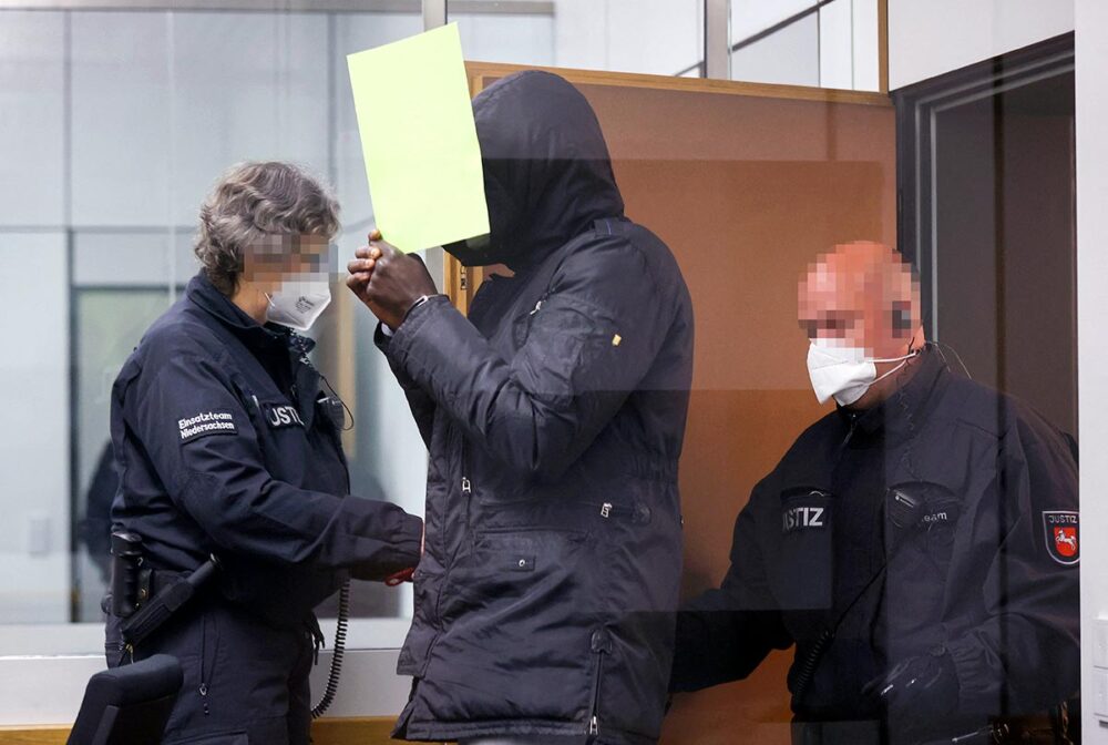 Le procès de Bai Lowe se déroule en Allemagne pour des crimes commis en Gambie. - Photo : Lowe entre dans la salle d'audience accompagné de policiers.