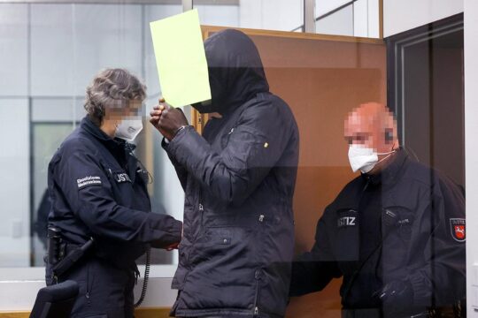 Le procès de Bai Lowe se déroule en Allemagne pour des crimes commis en Gambie. - Photo : Lowe entre dans la salle d'audience accompagné de policiers.