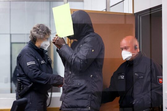 Bai Lowe is on trial in Germany for crimes committed in the Gambia. - Photo: Lowe enters the courtroom accompanied by police officers.