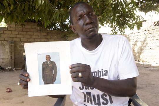 In The Gambia, victims of Yahya Jammeh's dictatorship are still waiting for reparations. Photo: The brother of a person who disappeared during Jammeh's regime shows a photo of him in uniform and wears a T-shirt calling for justice in The Gambia.