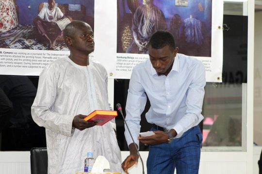 Ensa Badgie prepares to testify (book in hand) at a Gambia Truth Commission (TRCC) hearing, next to an employee