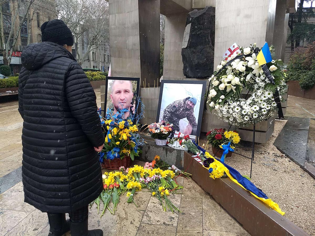 Une femme observe les photos de 2 soldats posées sur une pierre tombale près d'un drapeau ukrainien
