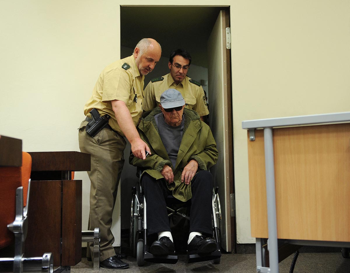 Defendant John Demjanjuk arrives in a wheelchair at court for his trial in Germany, assisted by two police officers.