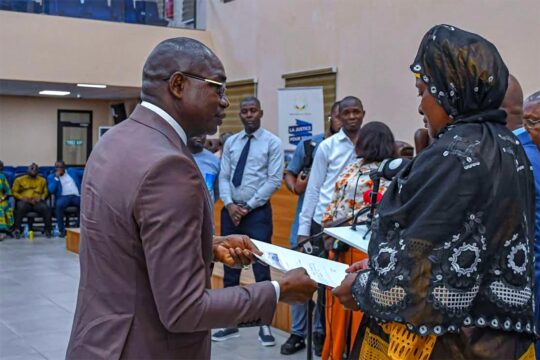 Justice in Guinea: reparations for victims of the 28 September 2009 massacre. Photo: A man in a suit hands a document to a woman in a courtroom.