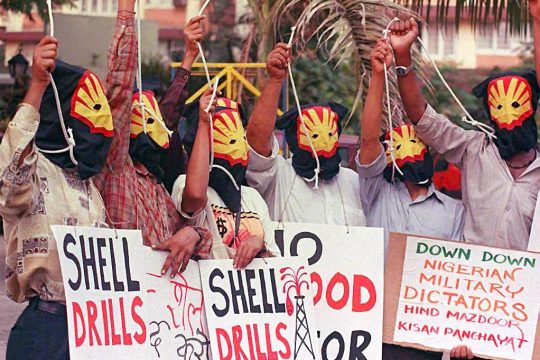 Masked protesters (Shell logo) raise their fists and hold up 