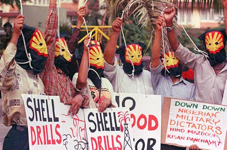 Des manifestants masqués (logo de Shell) lèvenet le poing et brandissent des pancartes "Shell drills".