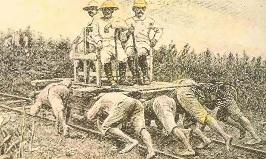 Illustration ancienne montrant des esclaves indonésiens qui poussent un chariot sur des rails. 3 colons armés sont assis sur un banc placé sur le chariot.