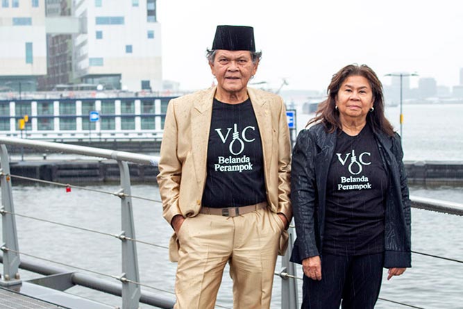 Jeffry Pondaag and Dida Pattipilohy pose in front of the Amsterdam Court of Appeal in the Netherlands. They are wearing the same black t-shirt that says "Belanda Perampok".