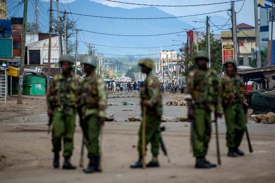 In the foreground: members of the riot police, armed and in military uniforms. In the background: people gathered in the street. Kisume (Kenya) in 2017.