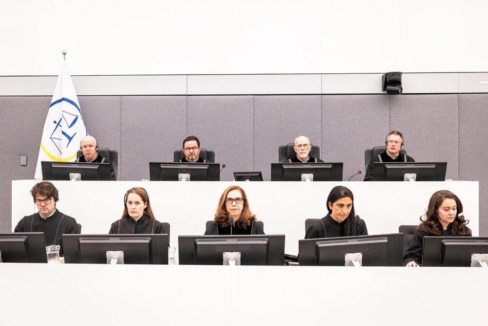 Le panel des juges des Chambres spécialisées du Kosovo délivrent leur verdict dans leur plus important procès, le 16 septembre 2026, à La Haye. Photo : © KSC Les Chambres spécialisés du Kosovo (KSC), une cour internationale de l'Onu basée à la Haye (Pays-Bas), vient de juger 4 personnalités kosovares inculpées pour crimes de guerre, dont l'ex-président Hashim Thaçi. Photo : les 4 juges sont assis sur une estrade au-dessus de leurs 5 assistants dans un décor blanc très lumineux et froid.