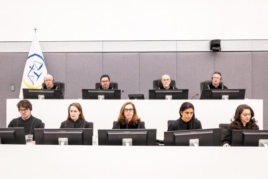 Les Chambres spécialisés du Kosovo (KSC), une cour internationale de l'Onu basée à la Haye (Pays-Bas), vient de juger 4 personnalités kosovares inculpées pour crimes de guerre, dont l'ex-président Hashim Thaçi. Photo : les 4 juges sont assis sur une estrade au-dessus de leurs 5 assistants dans un décor blanc très lumineux et froid.