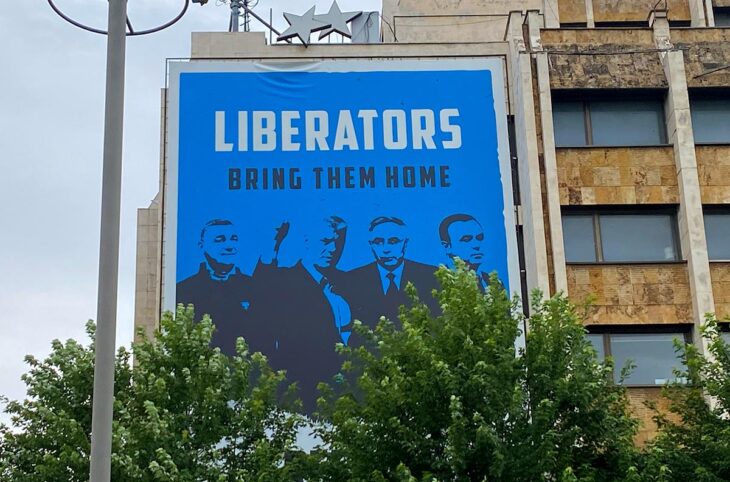 Les Chambres spécialisées du Kosovo (KSC) : un tribunal spécial (basés à La Haye) pour les crimes de guerre et crimes contre l'humanité commis par les forces kosovares durant la guerre contre la Serbie, dont l'objet et le fonctionnement sont controversés. Photo : une grande affiche bleue est accrochée à un immeuble. Il y est écrit :