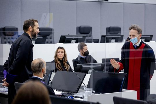 Salih Mustafa's lawyer (Julius von Bone) faces and greets prosecutor Jack Smith during the trial in The Hague for the allegated war crimes commited by Mustafa in Kosovo.