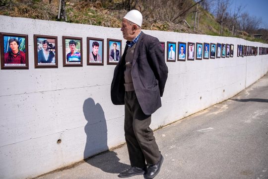 An old man looks at photos of war victims on a wall in Kosovo.