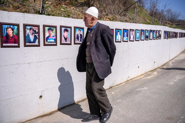 An old man looks at photos of war victims on a wall in Kosovo.