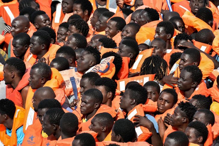 Many people wearing life jackets wait untel the are rescued from a rubber boat