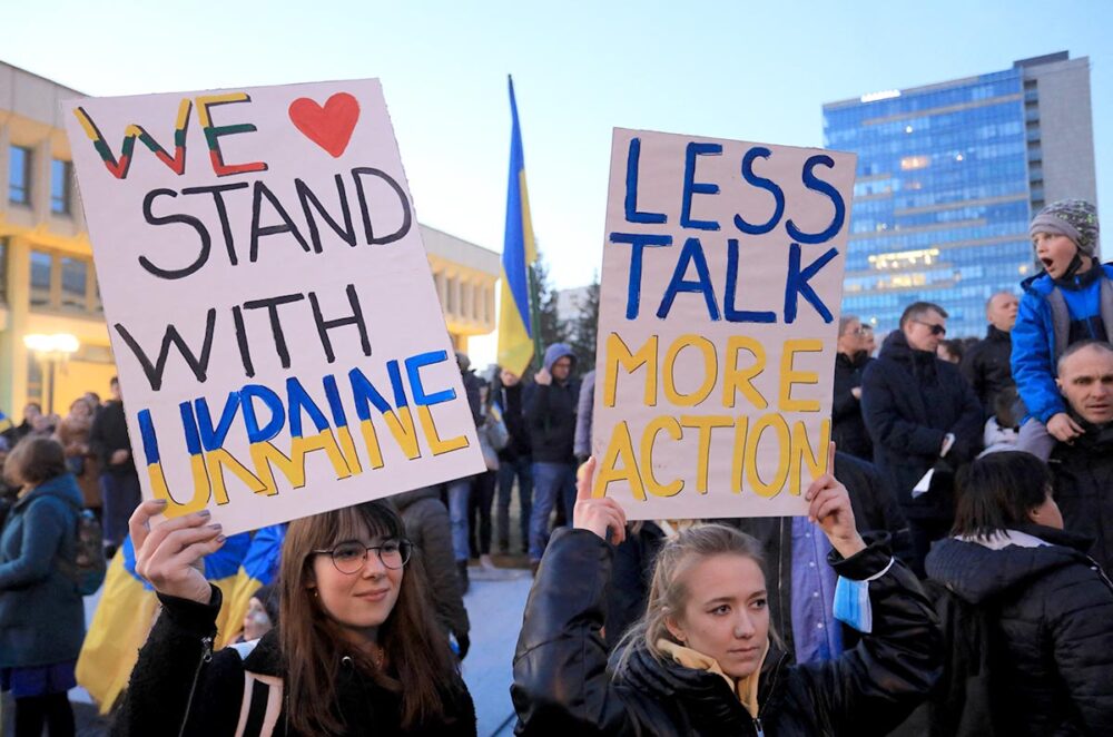 Demonstration in Vilnius (Lithuania). Two women hold signs saying 'We stand with Ukraine' and 'Less talk, more action'.