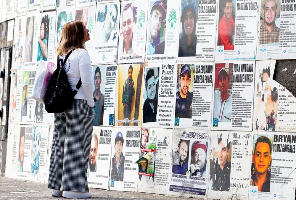 A mother looks at a portrait of her missing son at the Glorieta de los Desaparecidos (Roundabout of the Disappeared) on Mother’s Day in Guadalajara, in the state of Jalisco (Mexico), on 10 May 2026. Photo: © Ulises Ruiz / AFP Enforced disappearances in Mexico: when the UN gets involved. Photo: a mother searches for her missing son, looking at posters of missing persons on a wall in the street.