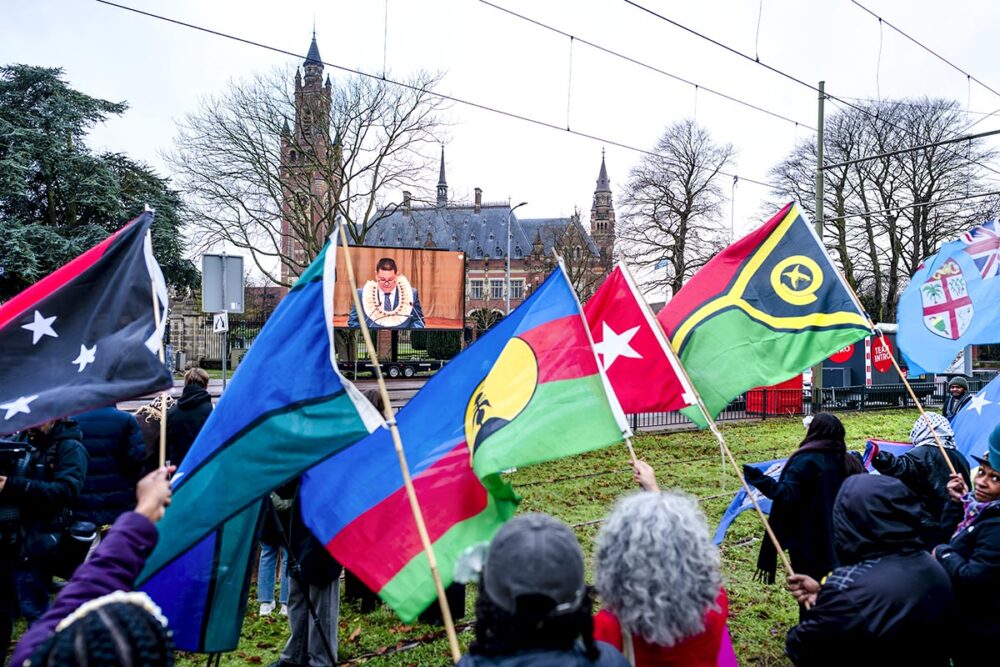 Climate justice at the International Court of Justice (ICJ) in The Hague (Netherlands). Photo: Demonstrators wave flags in front of the Peace Palace, calling on states to take responsibility for global warming.