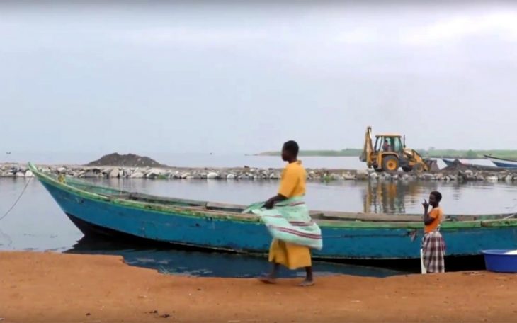 Au premier plan, un bateau et des habitants. En arrière-plan, une pelleteuse.