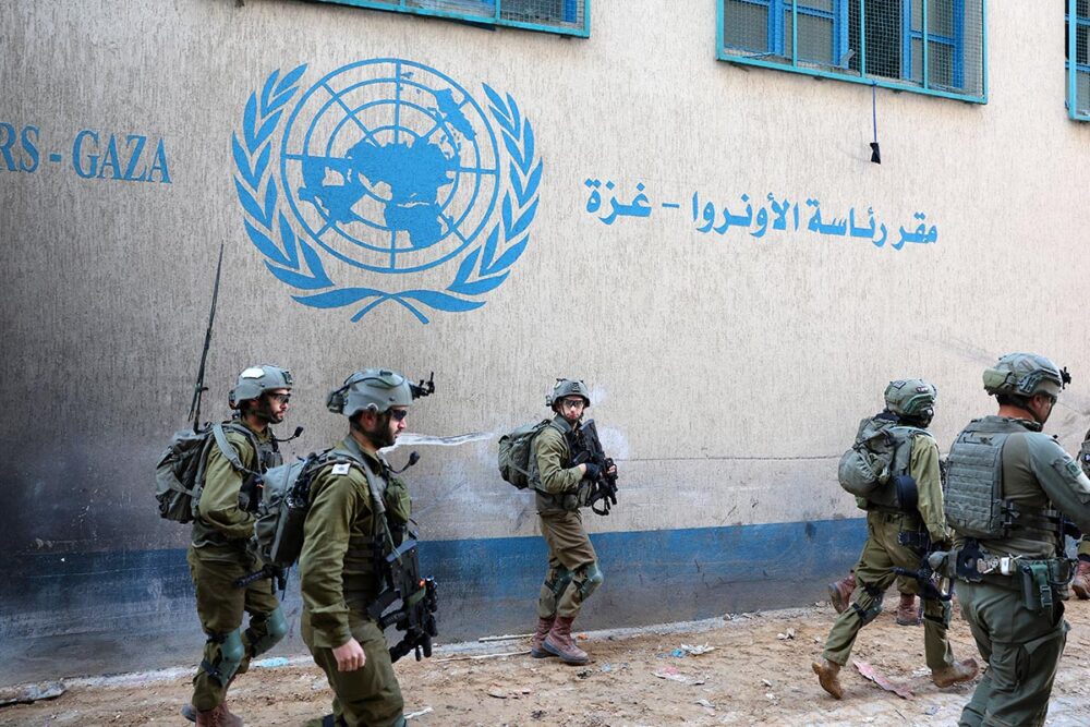 A Gaza (Palestine), des soldats étrangers ou binationaux officiant dans l'armée israélienne sont accusés de crimes de guerre. Photo : des soldats israéliens patrouillent dans une rue de Gaza City, passant devant un mur sur lequel est peint un logo de L'Onu et une inscription en arabe.