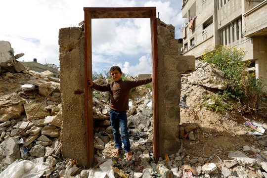 Enfant palestinien se tenant devant une porte exempte de murs autour, au milieu des ruines